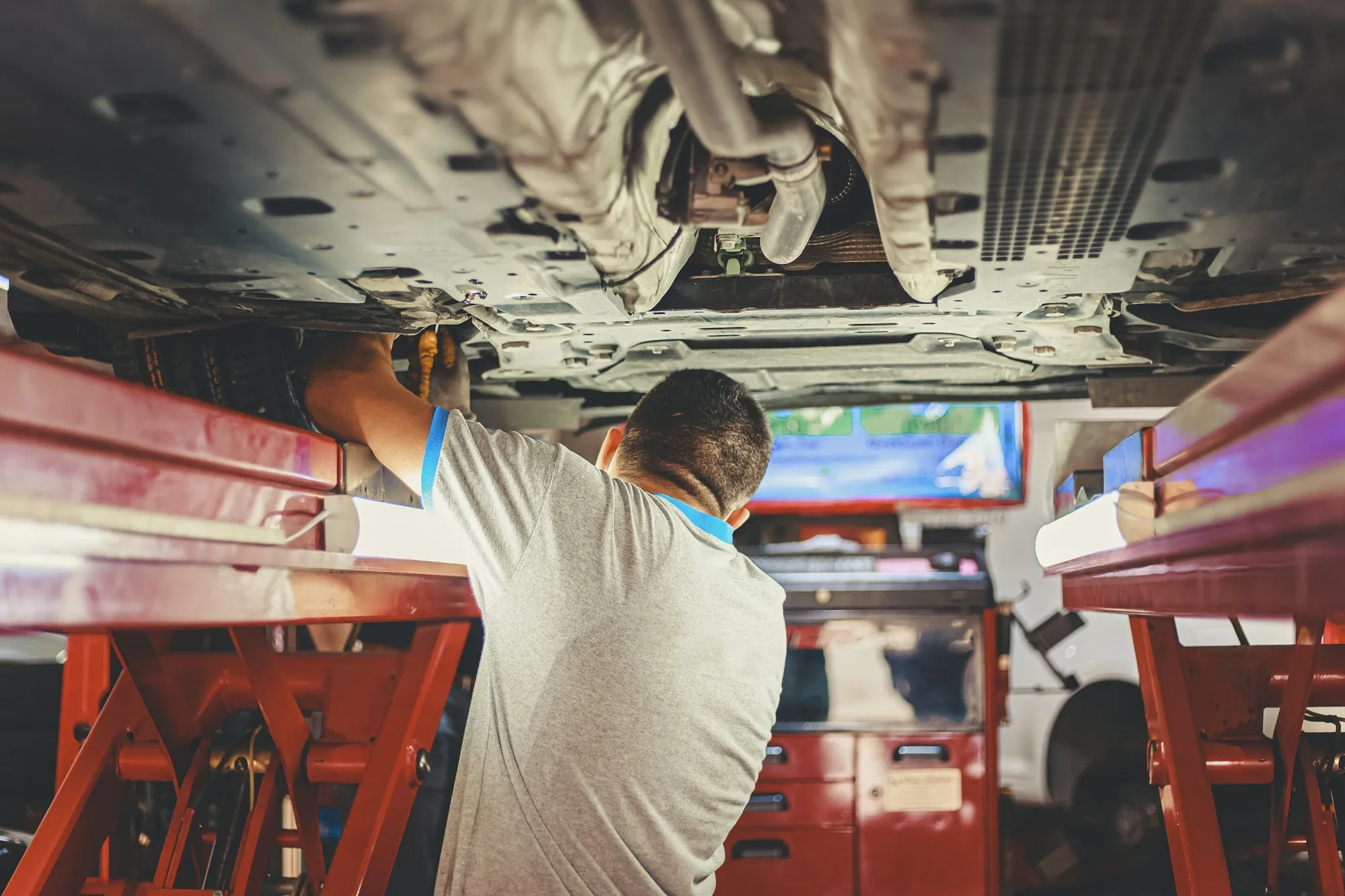 Mechanic in a gray shirt working beneath a car raised on a lift